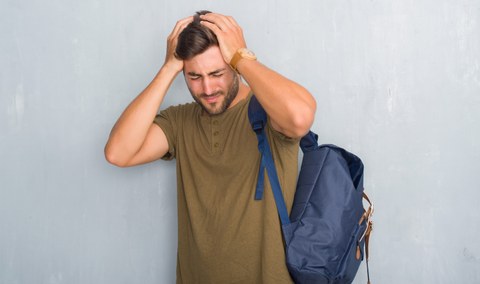 Foto einer Person mit Rucksack, die die Hände an den Kopf und das Gesicht vor Schmerz verzerrt