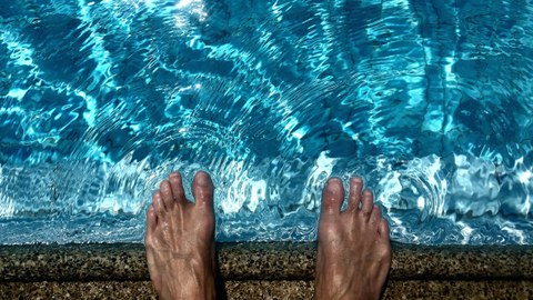 Feet which stand next to a swimming pool