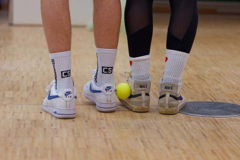 Tennisball wird zwischen Schuhaußenseiten von zwei Personen gehalten