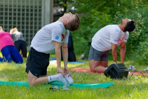 Zwei Schüler:innen des Physiotherapeutischen Lehrzentrums die ihre Hände im Rahmen einer Übung auf ihre Fersen stützen und den Blick in den Himmel richten