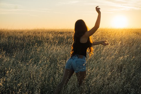 beschwingte Frau auf einem Feld bei Sonnenuntergang