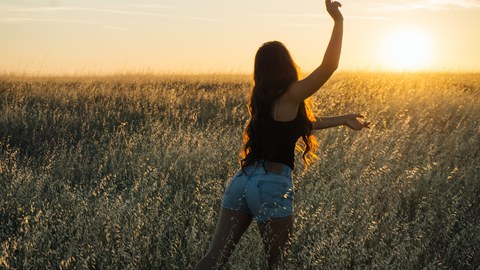 beschwingte Frau auf einem Feld bei Sonnenuntergang