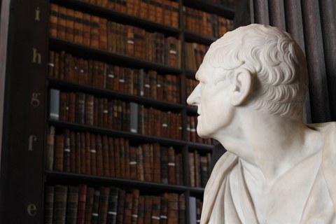 Statue zu Büchern im Hintergrund blickend