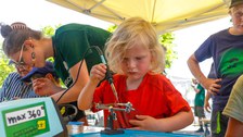 Ein Kleinkind mit blonden langen Haaren arbeitet mit Lötkolben an einem Stand bei den Zukunfstagen Hirschfelde