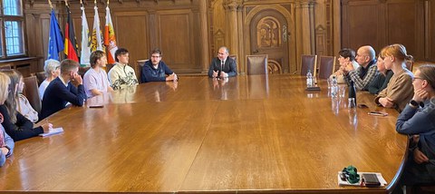 In einem holzgetäfelten Raum sitzen an einem sehr großen Tisch 10 Personen im offiziellen Gespräch