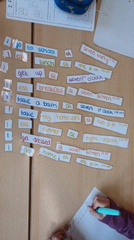 Vogelperspektive: Auf einem Tisch liegen englische Wortkarten in verschiedenen Farben. Eine Schülerin schreibt in ihr Heft.