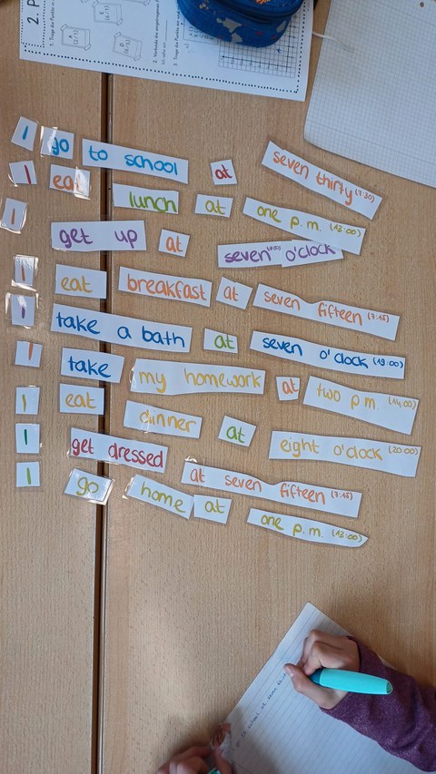 Vogelperspektive: Auf einem Tisch liegen englische Wortkarten in verschiedenen Farben. Eine Schülerin schreibt in ihr Heft.