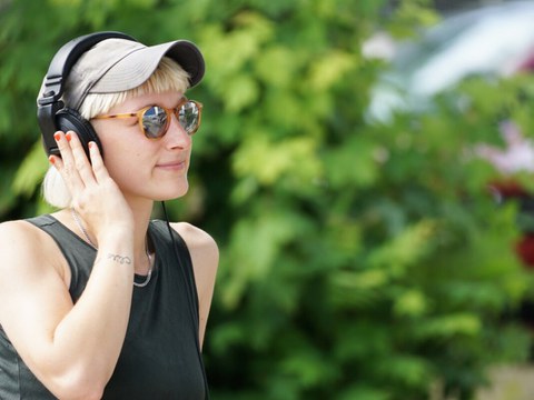 Foto einer Frau, die auf dem TU Campus mit Kopfhörern Musik oder einen Podcast hört.