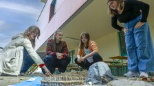 Zwei Studentinnen und zwei Schülerinnen erstellen vor der Schule Modelle von Küstenverläufen mit Sand und anderen Materialien.