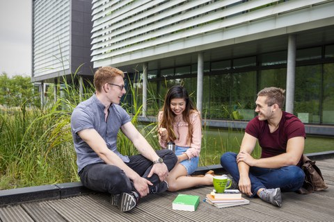 Studierende sitzen am Teich des Informatikgebäudes
