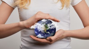 Bildausschnitt einer Frau, die ein Planetenmodell der Erde in beiden Händen hält.