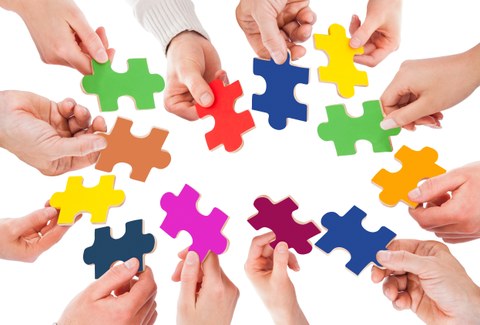 Foto von vielen Händen, die unterschiedliche farbige Puzzleteile in den Händen halten und einen Kreis bilden