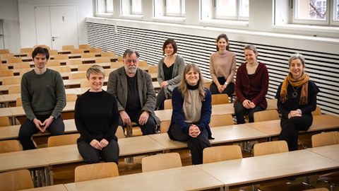 Mitarbeitende der Professur sitzen auf Bankreihen verteilt und gucken in geradeaus in die Kamera.