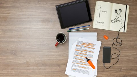 Schreibtischaufsicht mit Tablet, Kaffee, Ausdrucken, Stiften und einem aufgeschlagenen Buch