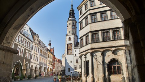 Blick durch einen weiten Torbogen auf den Platz einer mittelalterlichen Stadt. Es ist der Blick vom Laubengang zum Untermarkt in Görlitz.