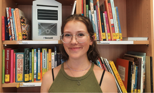 Foto: SHK Julia Carola Seifert lächelnd vor dem Bücherregal der LuFo