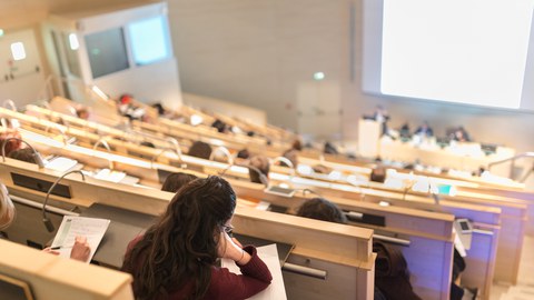 Studierende sitzen in einem Hörsaal und machen Notizen während einer Vorlesung.