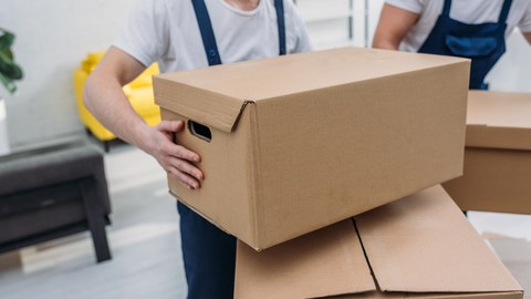 Bild von zwei Personen, die Umzugskartons tragen und transportieren.