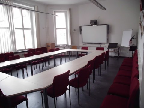 Abgebildet ist der Raum mit Tischen und Stühlen sowie der interaktiven Tafel.