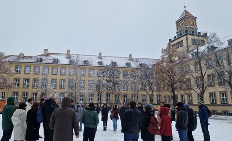 Menschen stehen in einem Kreis auf dem Hof des Weberplatzes, dieser ist verschneit.