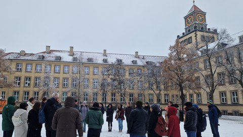 Menschen stehen in einem Kreis auf dem Hof des Weberplatzes, dieser ist verschneit.