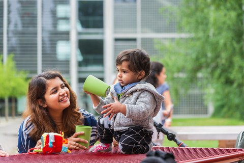 Eine Frau und ihr Kleinkind sitzen am Imbisstisch am Hörsaalzentrum und spielen mit Bechern.