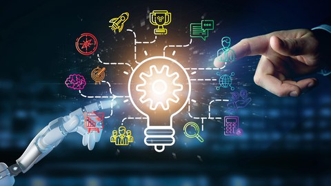 Foto einer menschlichen Hand im oberen rechten Bildrand und einer Roboterhand im unteren linken Bildrand. Beide Händen zeigen mit dem Zeigefinger auf eine visualisierte Darstellung einer Glühbirne mit verschiedenen Icons, die um diese herum angeordnet sin