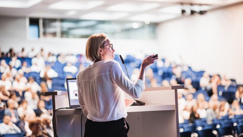 Foto einer Person, die einen Vortrag hält und vor einem großen Publikum steht