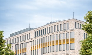 Es wird das Gebäude Münchner Platz 1 dargestellt, teilweise hat es vergoldete Fensterbereiche.