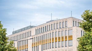 Es wird das Gebäude Münchner Platz 1 dargestellt, teilweise hat es vergoldete Fensterbereiche.