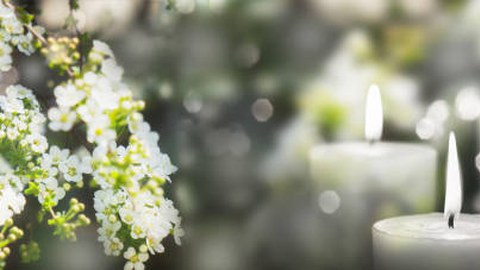 Abgebild ist ein Blütenzweig mit weißen Blüten und rechts daneben eine brennende weiße Kerze.