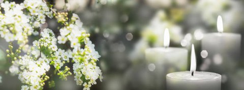 Abgebild ist ein Blütenzweig mit weißen Blüten und rechts daneben eine brennende weiße Kerze.