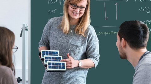 Berufschullehrerin erklärt zwei Studierenden anhand eines Modelles die Funktionsweise von Solarpanels