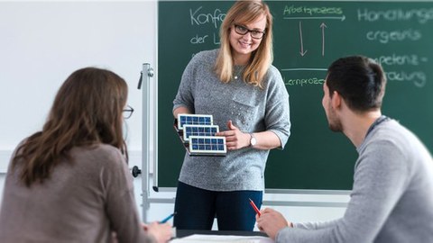 Berufsschullehrerin erklärt zwei Auszubildenden ein Solarpanel