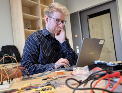 Niculin, ein blonder junger Mann, sitzt an einem Tisch und schaut konzentriert auf seinen Laptop.