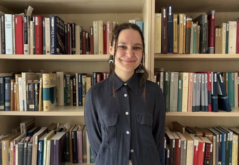 Auf der Abbildung ist Jule Strecker zu sehen, wie sie vor einem Bücherregal steht.
