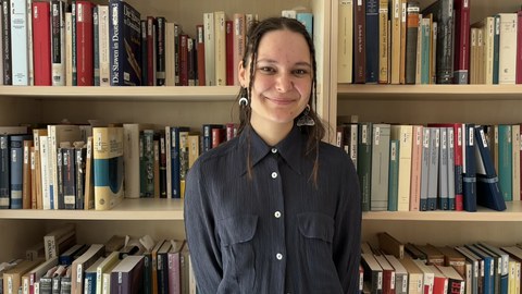 Auf der Abbildung ist Jule Strecker zu sehen, wie sie vor einem Bücherregal steht.
