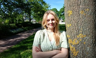 Auf dem Bild ist eine lächelnde blonde Frau mit braunen Augen zu sehen. Sie trägt ein grünes Kleid.