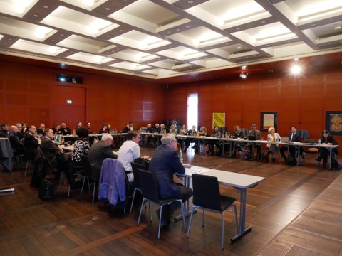 A view of the Klemperer Hall at the SLUB. Men and women are seated at tables arranged in a U-shape.