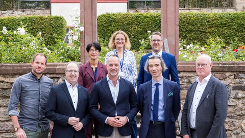 Gruppenfoto von acht Personen vor einem steinerne Torbogen und einem historischen rot-weißen Gebäude im Hintergrund. Im Vordergrund stehen Sebastian Macho, Markus Harzenetter, Julius Wagner, Mirko Breitenstein und Ingo Schon, dahinter auf den Stufen Doris Moos, Gaby Lindenmann-Merz und Christoph Degen.