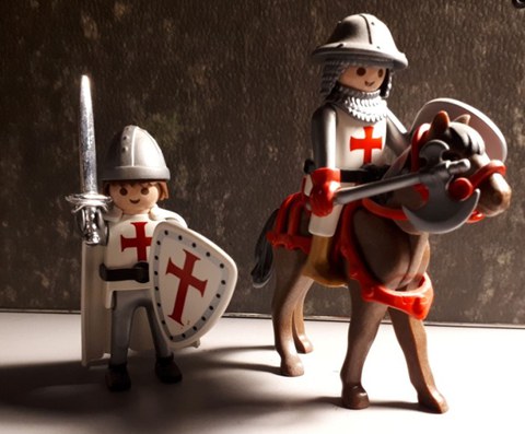 Auf dem Bild sind zwei Playmobil-Tempelritter zu sehene, die anhand des roten Kreuzes auf weißem Hintergrund  erkennbar sind. Ein Ritter reitet dabei auf einem Pferd, während der andere mit Schwert und Schild bewaffnet ist.