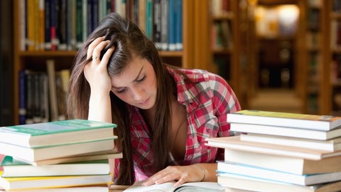 Frau beim Lernen zwischen Bücherstapeln