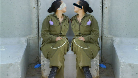 Two women sit facing each other on a concrete block. It is the same woman, the image is mirrored. She is wearing overalls, her hair is dark and tied back in a bun. There is a purple object in her breast pocket and she is holding a thin white object in her hand, reminiscent of a cable tie. Her eyes are blindfolded with a scarf (left) and a black strip covers her eyes (right). 