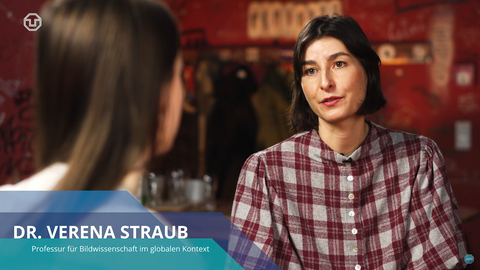 Screenshot aus einem Video. Im Bild eine Person von schräg hinten, eine Person von vorn. Binde, zweizeilig: "DR. VERENA STRAUB. Professur für Bildwissenschaft im globalen Kontext."