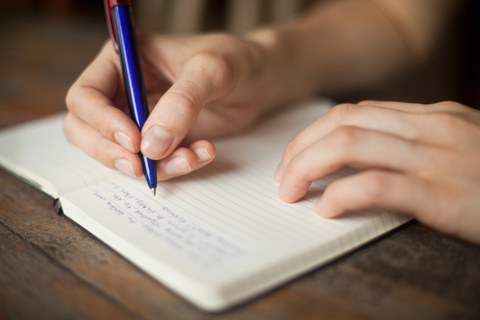 Foto zeigt ein geöffnetes Notizbuch und ein Hand mit einem Stift