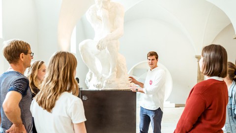 Foto, in dem ein Mann vor einer Menschengruppe steht und etwas über eine Statue daneben erzählt