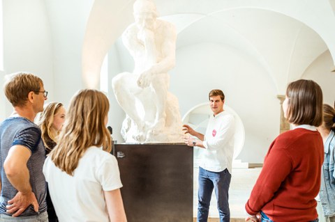 Foto, in dem ein Mann vor einer Menschengruppe steht und etwas über eine Statue daneben erzählt