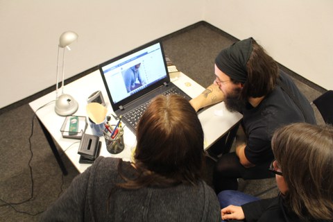 Bild von drei Personen, welche einen Laptop auf einem Tisch betrachten