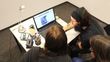 Bild von drei Personen, welche einen Laptop auf einem Tisch betrachten