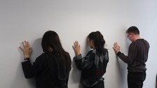 drei Personen stehen frontal zur Wand und haben Stirn und gehobene Handflächen an die Wand gelehnt